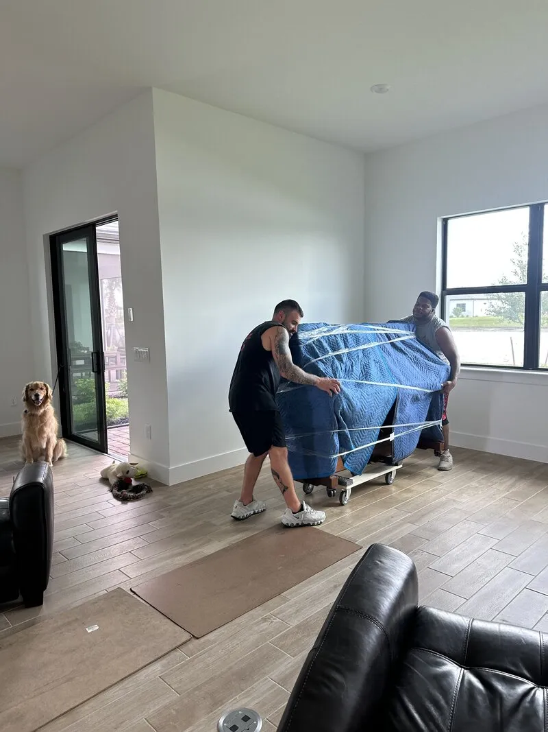 Two movers carrying a blanket-wrapped piece of furniture through a bright new home